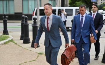 Un homme portant un costume bleu va le long d'un trottoir tout en portant un sac en cuir dans une main.