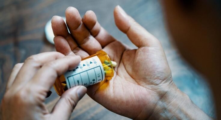 Fermement d'une main mâle tenant une bouteille de pilule, versant des médicaments à la main