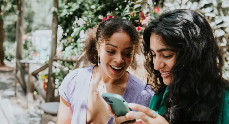 Deux jeunes femmes regardent le téléphone portable et sourient.
