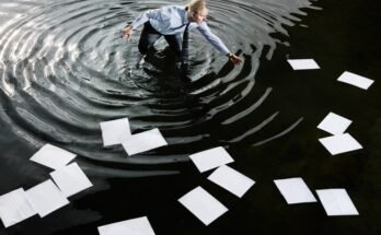 Un homme intelligemment habillé pataugeant le genou profondément dans l'eau noire, atteignant la feuille liquide de papier blanc A4.