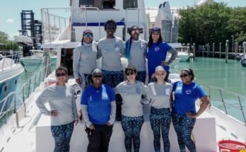 Un groupe de jeunes femmes compense une photo sur un bateau dans une marina, avec le drapeau américain, le drapeau de la fierté et les drapeaux de matériaux de vie noire