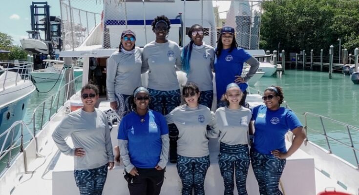Un groupe de jeunes femmes compense une photo sur un bateau dans une marina, avec le drapeau américain, le drapeau de la fierté et les drapeaux de matériaux de vie noire
