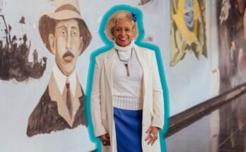 Un portrait de Sônia Guimarães, mis en évidence en bleu, debout devant une murale