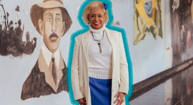 Un portrait de Sônia Guimarães, mis en évidence en bleu, debout devant une murale
