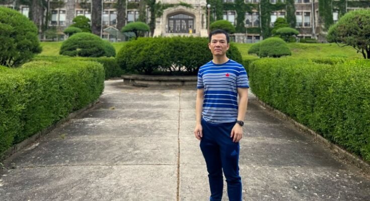 Zhicheng Lin se tenait sur un chemin à l'extérieur d'un bâtiment universitaire habillé par Efvy.