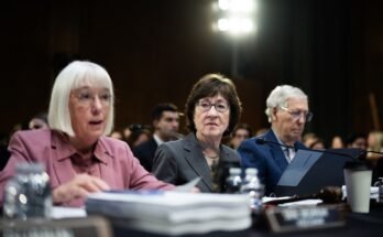 Trois personnes assises à une table recouverte de tas de papier.