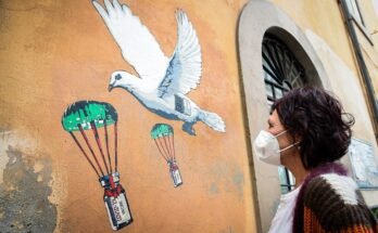La femme aux cheveux noirs et au masque regarde une peinture murale avec des pigeons et des flacons de vaccin coiffés qui sont en cours de réussite.