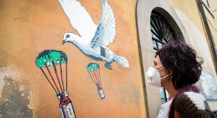 La femme aux cheveux noirs et au masque regarde une peinture murale avec des pigeons et des flacons de vaccin coiffés qui sont en cours de réussite.