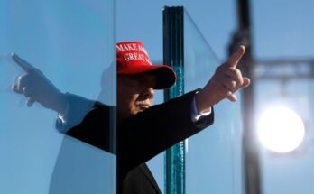Donald Trump porte un chapeau rouge et pointe son doigt.