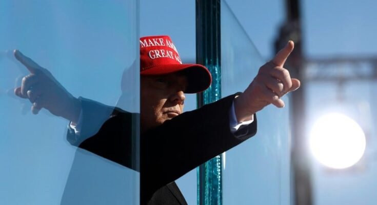 Donald Trump porte un chapeau rouge et pointe son doigt.